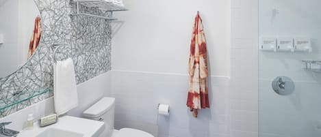 A modern bathroom with a glass shower enclosure, a white toilet, a sink with a soap dispenser, and a towel rack with a towel.