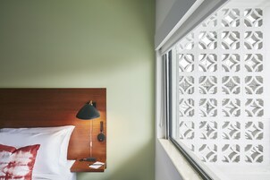 A hotel room with a wooden headboard, a black lamp, and a window with a decorative screen.