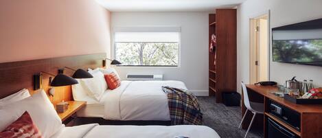 Une chambre d’hôtel avec deux lits, un bureau doté d’un micro-ondes, une télévision et une fenêtre donnant sur des arbres.