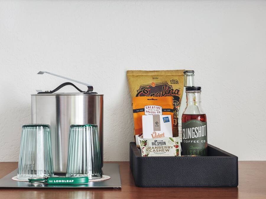 A kitchen setup with a kettle, two glasses, a bag of snacks, and a bottle of Slingshot coffee.