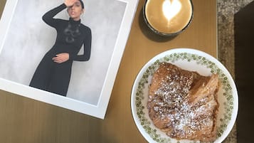 Una revista titulada 'Cereal' sobre una mesa de madera, una taza de café con un diseño de corazón, y un plato de comida.