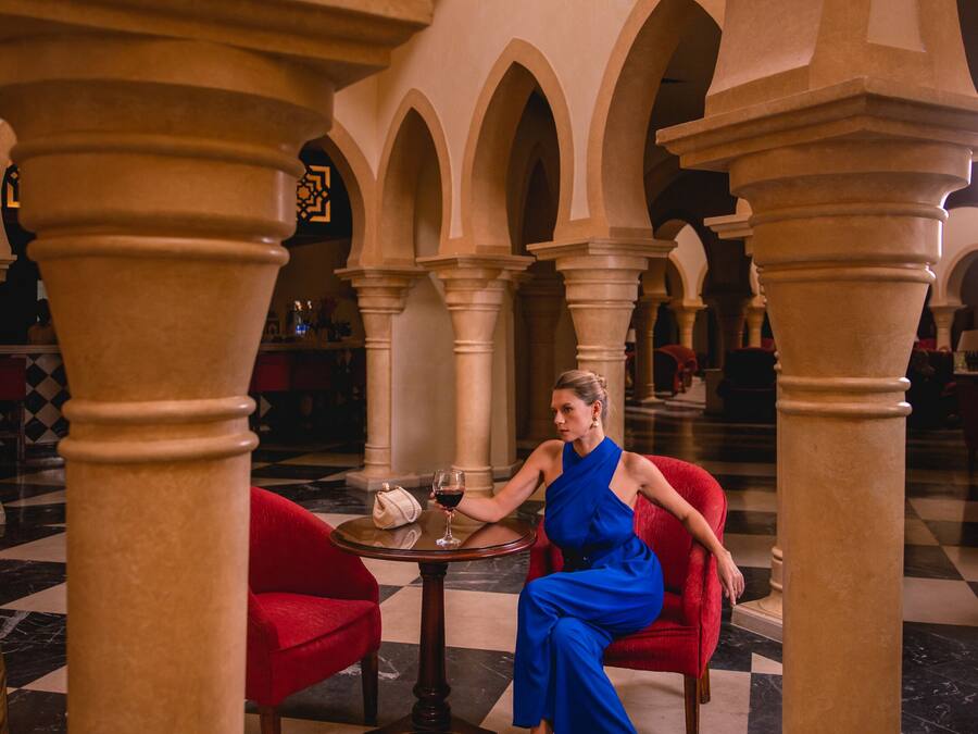 Una mujer sentada en una mesa en un vestíbulo lujoso con pisos de mármol y arquitectura clásica.