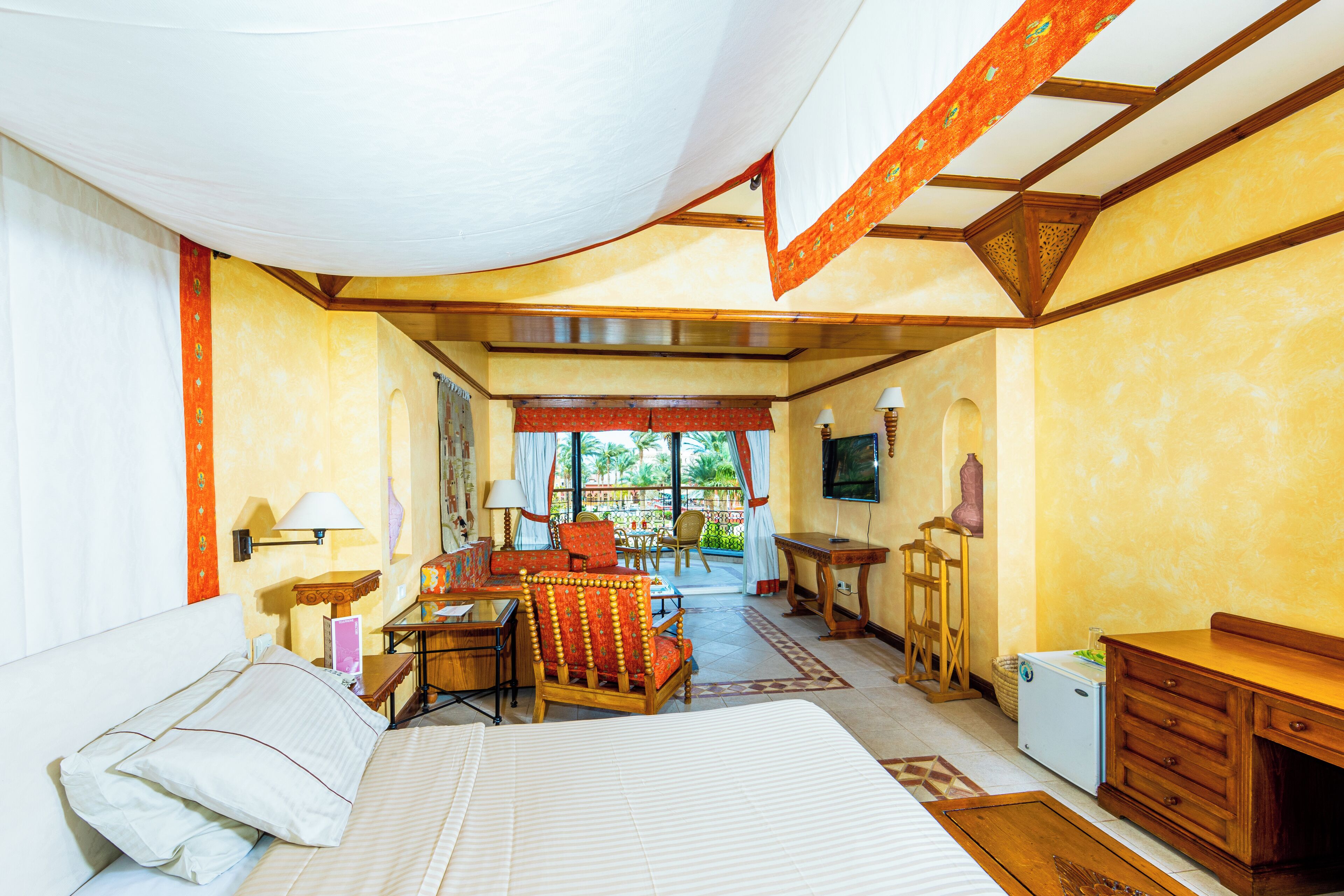 A hotel room with a bed, a desk, a chair, a TV, and a view of the outside.