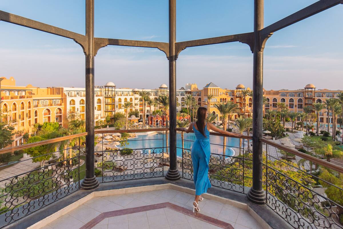 Eine Frau steht auf einem Balkon mit Blick auf einen Pool und Hotelgebäude.