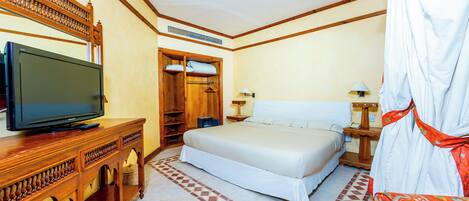 A hotel room with a bed, a television on a wooden cabinet, a wardrobe, a bedside table with a lamp, and a patterned rug.