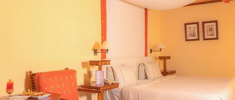 Habitación de hotel con cama, una silla, una mesita con bebidas y aperitivos, y dos lámparas de pared.
