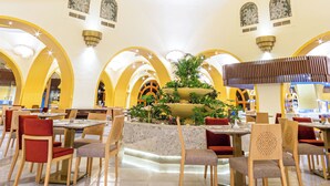 A spacious indoor area with multiple dining tables and chairs, a central decorative element on the ceiling, and arched architectural features. - The Grand Resort Hurghada (Hurghada)