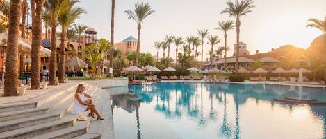 A resort pool area with palm trees, lounge chairs, and a building with domed architecture.