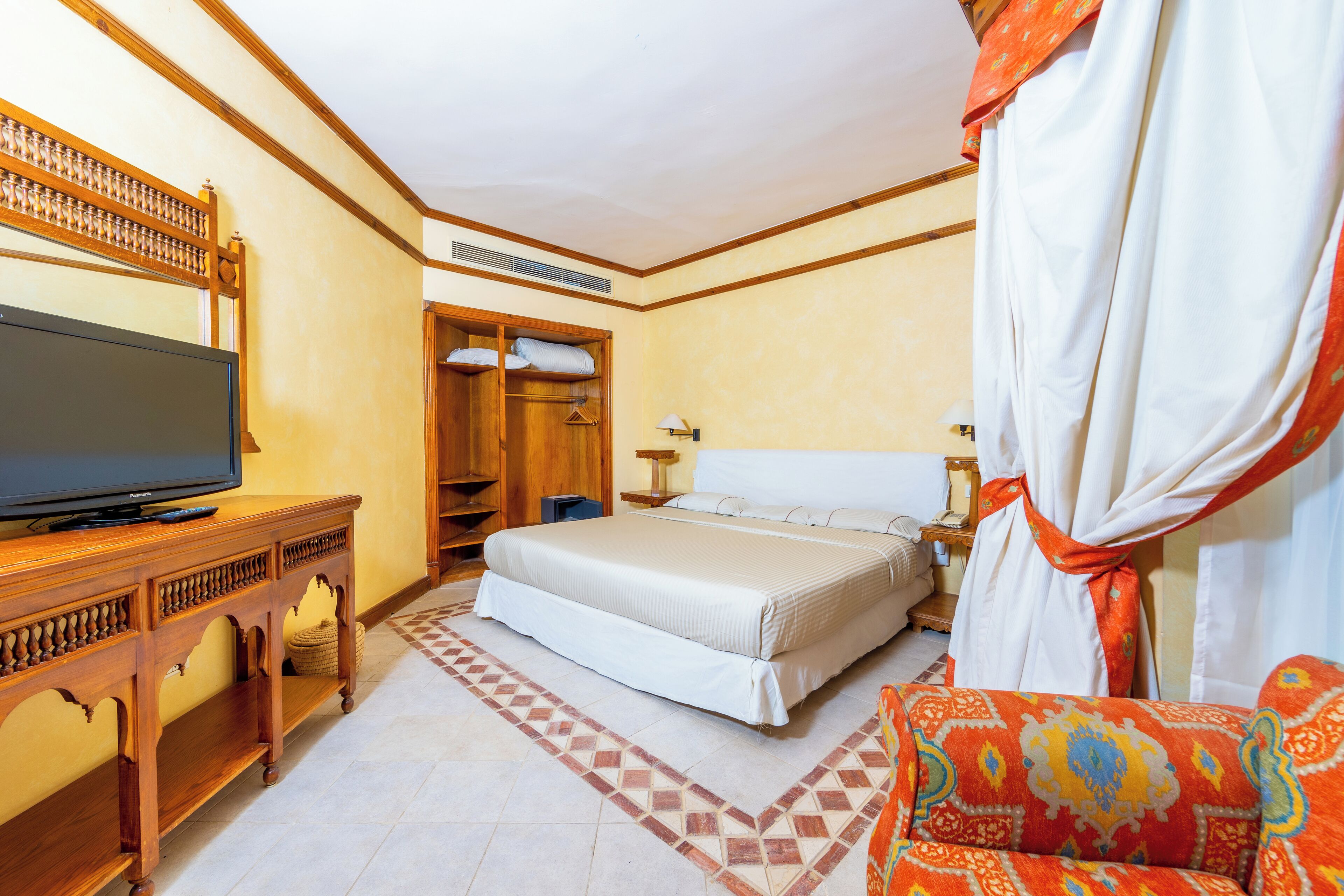 A hotel room with a bed, a TV on a wooden console, a wardrobe, and a patterned sofa.