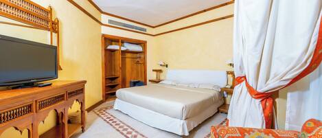 A hotel room with a bed, a TV on a wooden console, a wardrobe, and a patterned sofa.