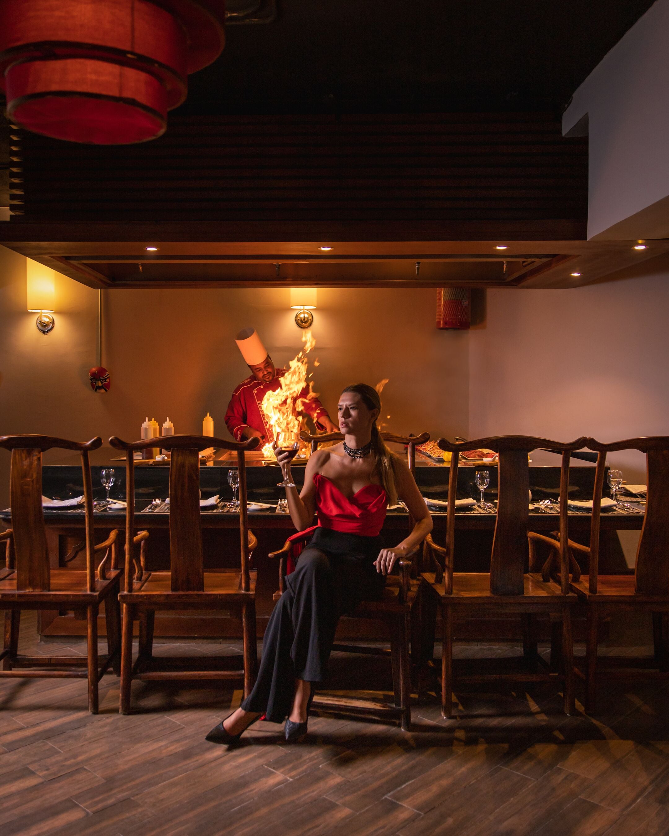 Una mujer sentada a una mesa en un restaurante tenuemente iluminado, con sillas y mesa de madera dispuestas para comer.