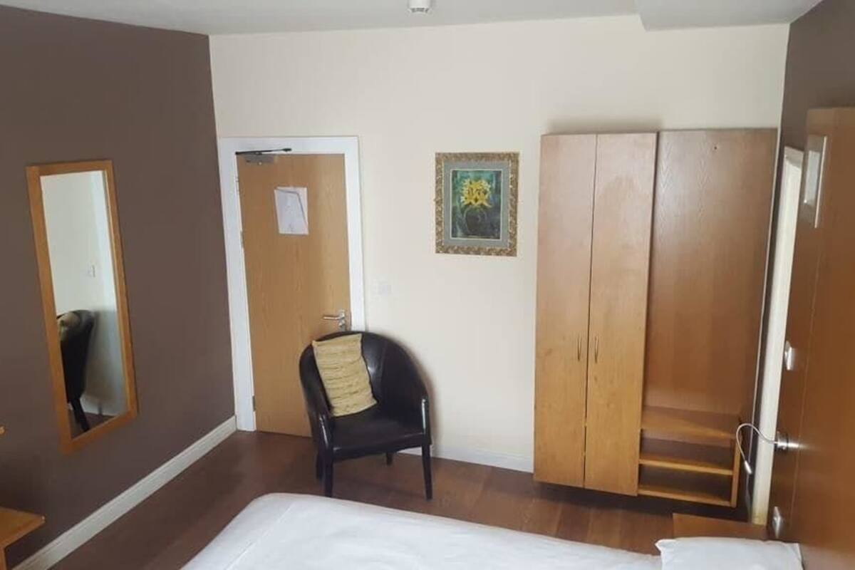 A hotel room with a bed, a chair, a wardrobe, a mirror, and a television.