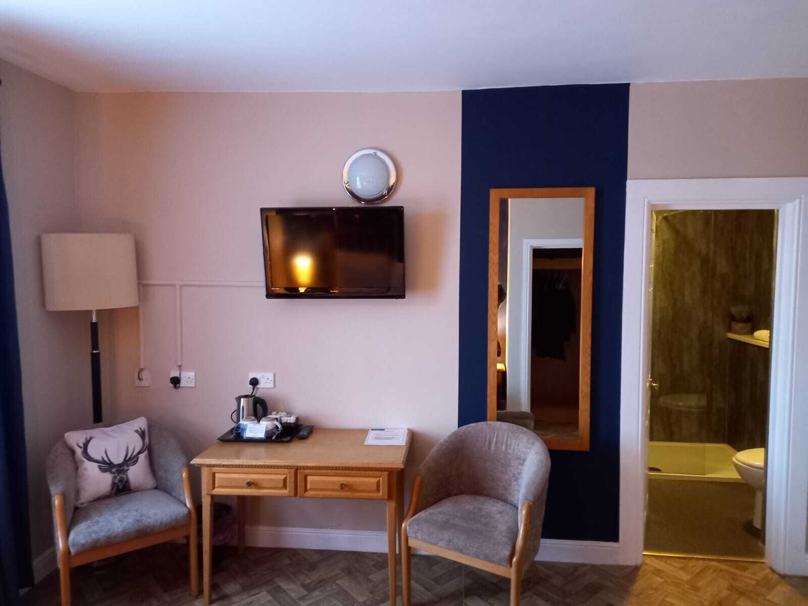 A small room with a desk, two chairs, a television, a mirror, and a bathroom visible through an open door.