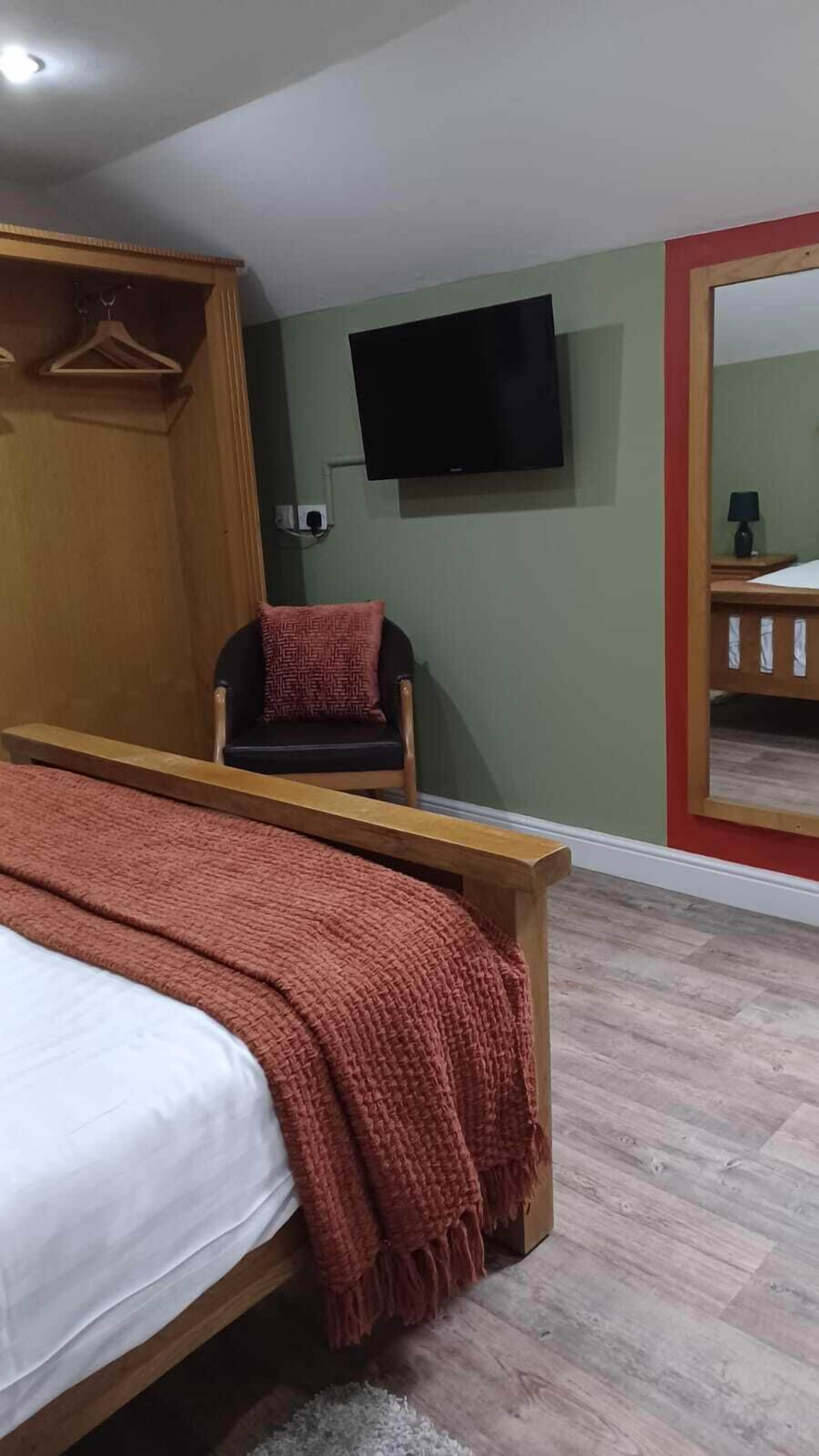 A bedroom with a bed, a chair, a television mounted on the wall, and a mirror.