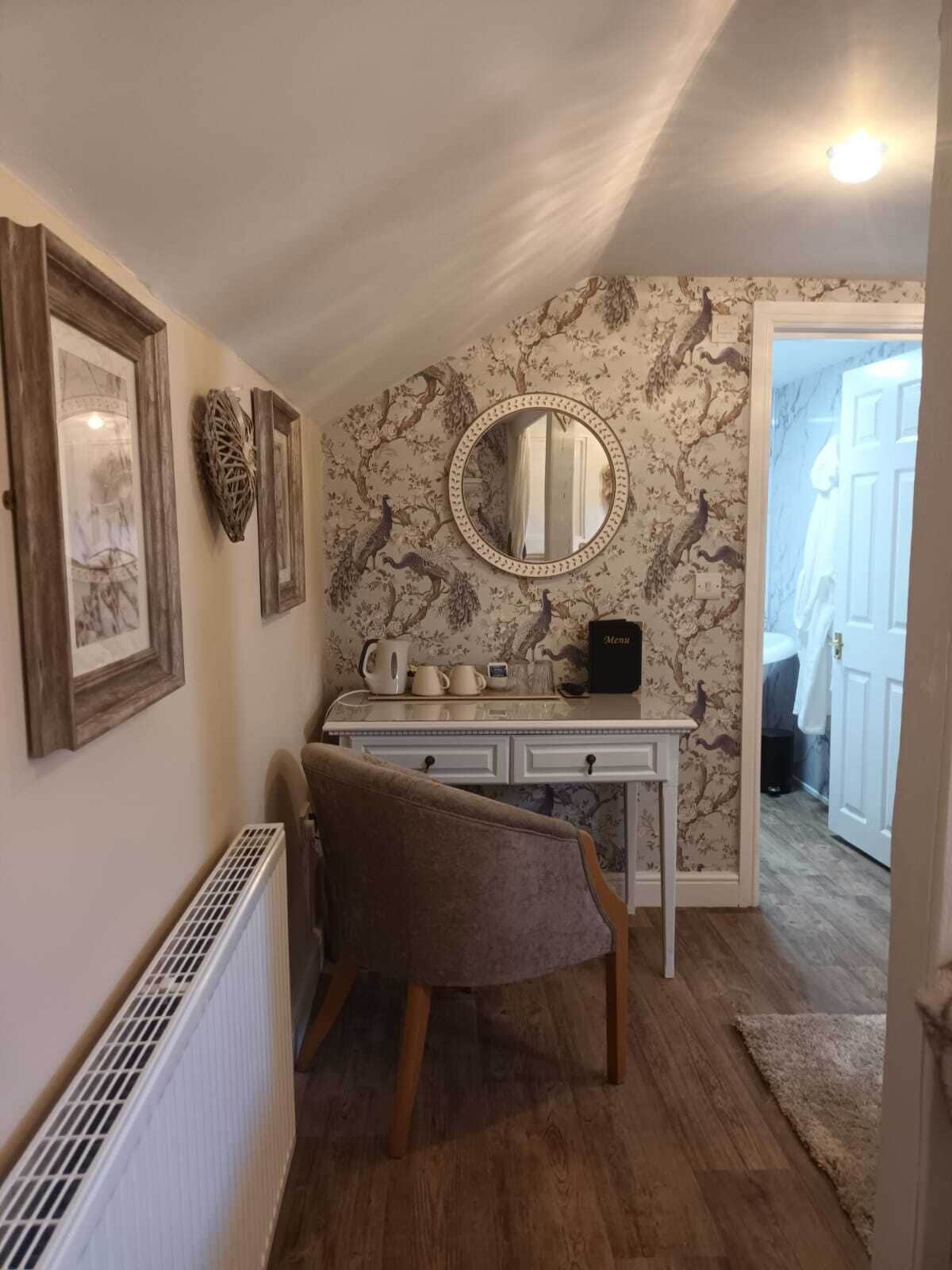 A room with a desk, chair, framed pictures, a mirror, and a radiator.