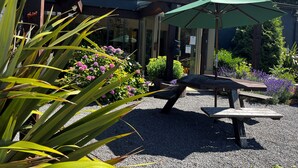 Een terras met een houten tafel en bankje, omringd door grind en verschillende planten.