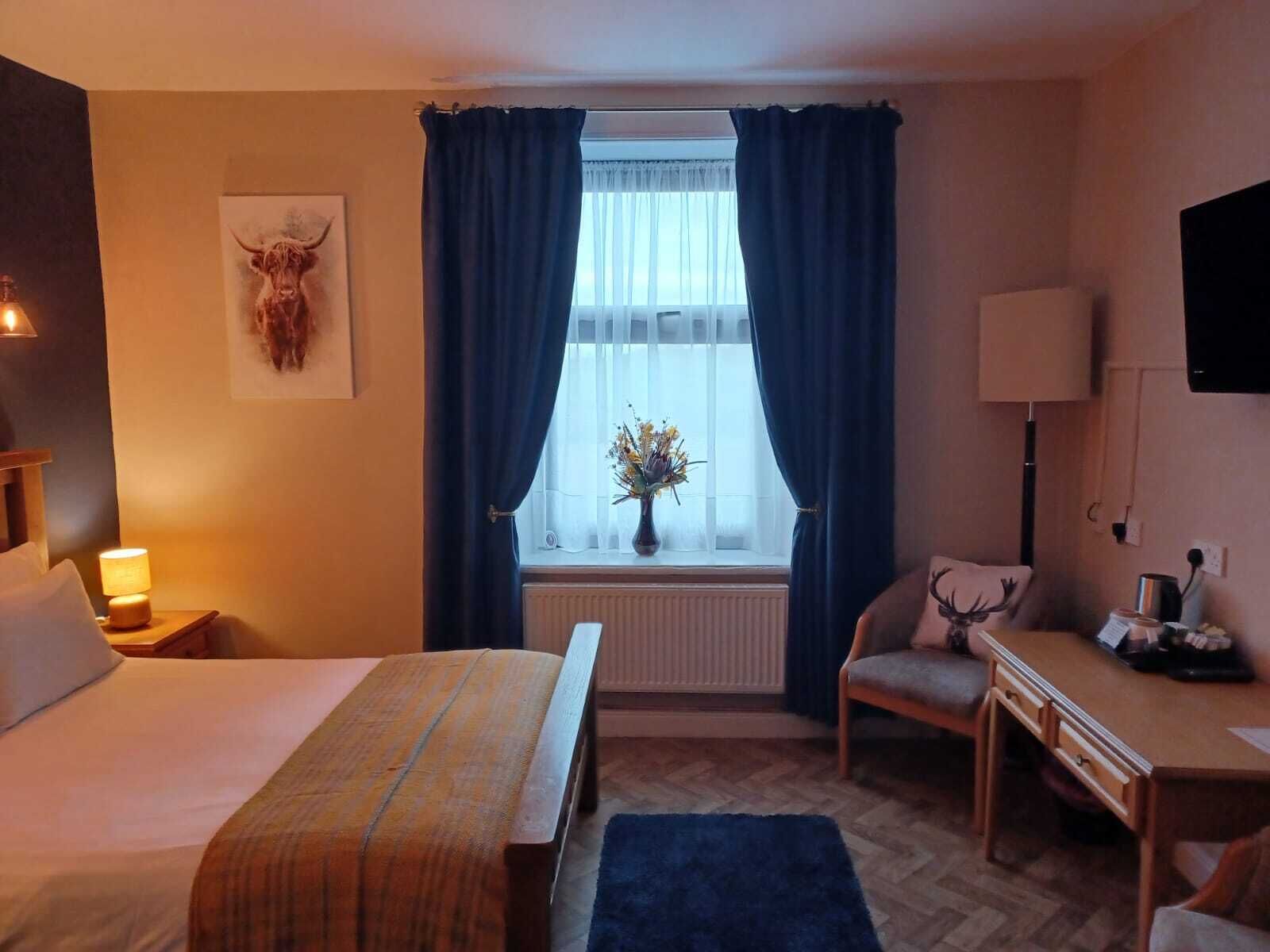 Ein Hotelzimmer mit Bett, Schreibtisch, Stuhl, Lampe, Fernseher und einem Fenster mit Vorhängen.