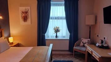 Una habitación de hotel con cama, escritorio, silla, lámpara, televisor y ventana con cortinas.