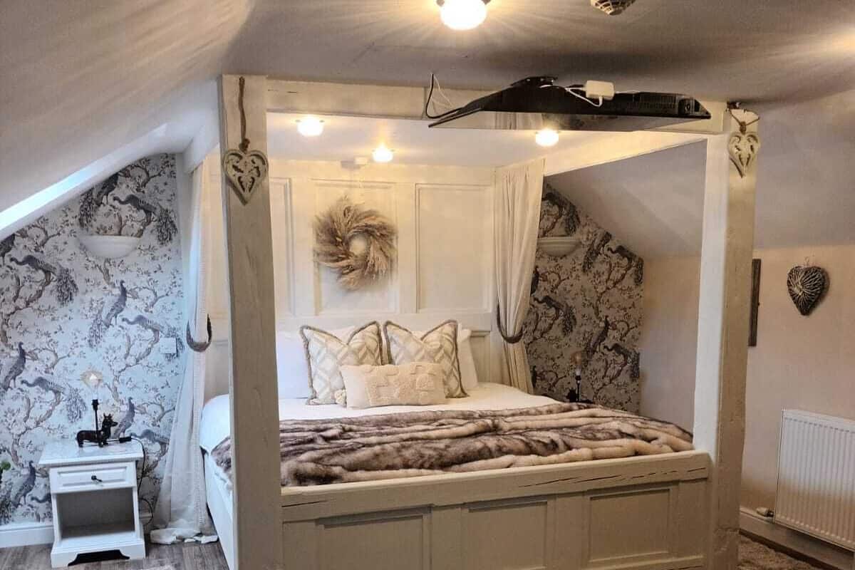 A bedroom with a four-poster bed, a nightstand, a radiator, and a decorative wreath on the wall.