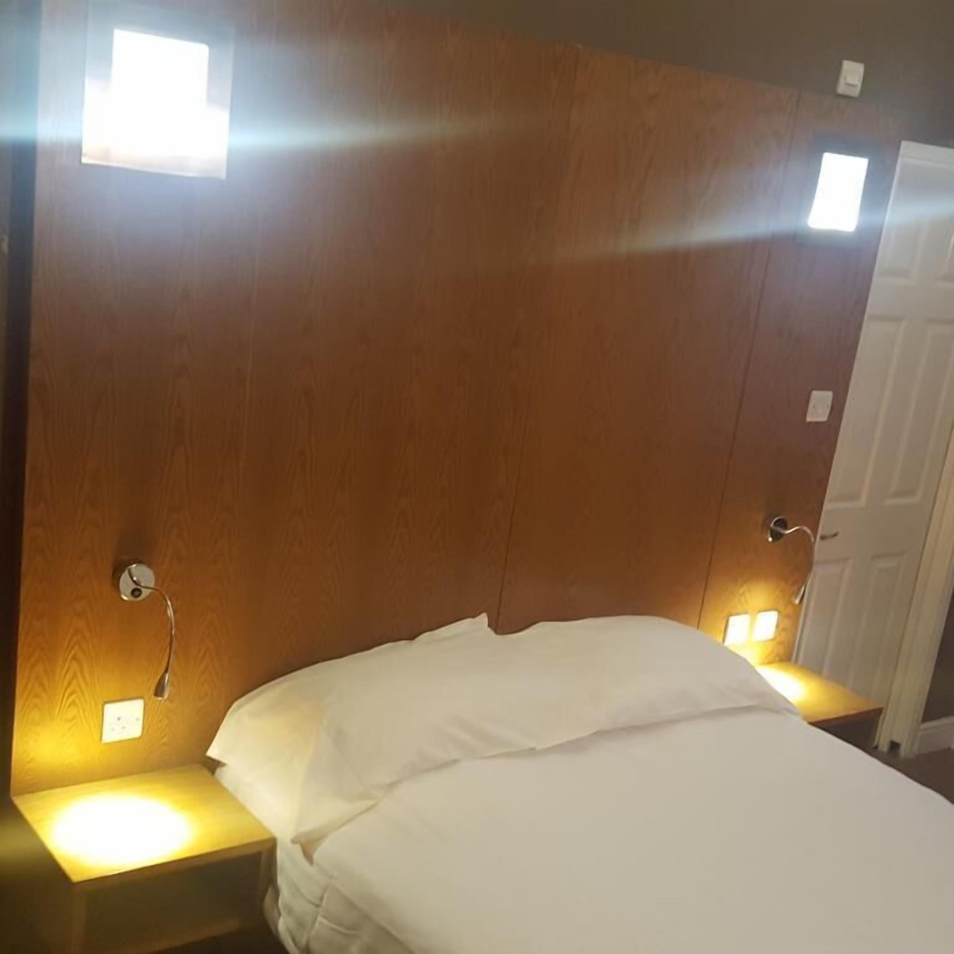 Quarto com cabeceira de madeira, duas luminárias de apoio e colcha branca.