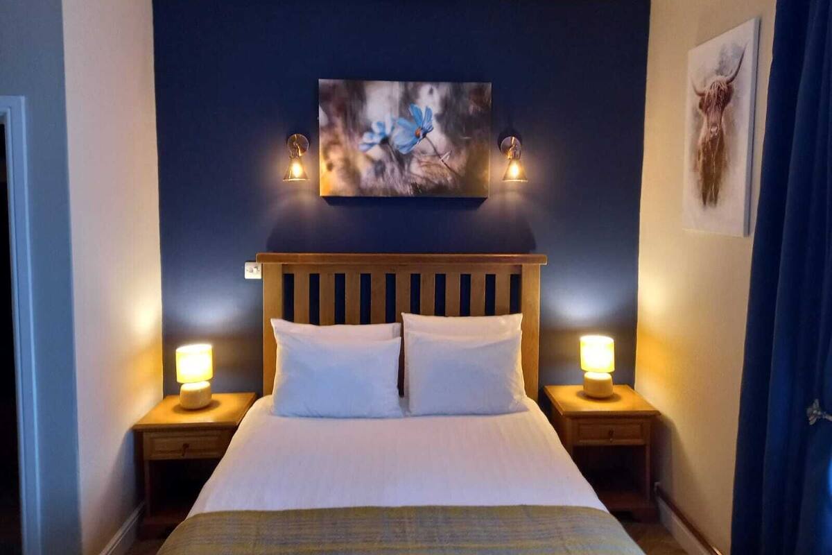 A bedroom with a wooden headboard, two bedside tables with lamps, and a painting above the bed.