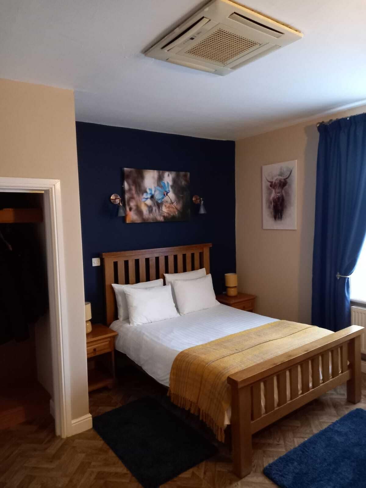 Ein Schlafzimmer mit einem hölzernen Bett, weißer Bettwäsche, einer blauen Wand und einem Deckenventil.
