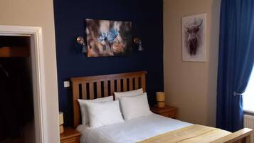 Ein Schlafzimmer mit einem hölzernen Bett, weißer Bettwäsche, einer blauen Wand und einem Deckenventil.