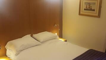 Een hotelkamer met een bed, nachtkastje, wandlamp en een lijst met een afbeelding.