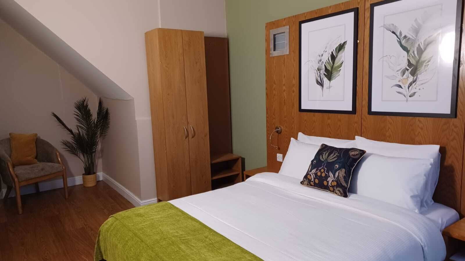 A bedroom with a bed, a wardrobe, a chair, and a potted plant.