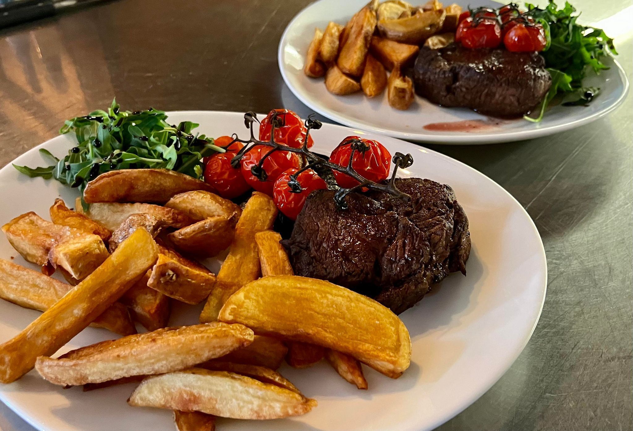 Dos platos de comida, uno con filete y papas fritas, el otro con filete y papas al horno.