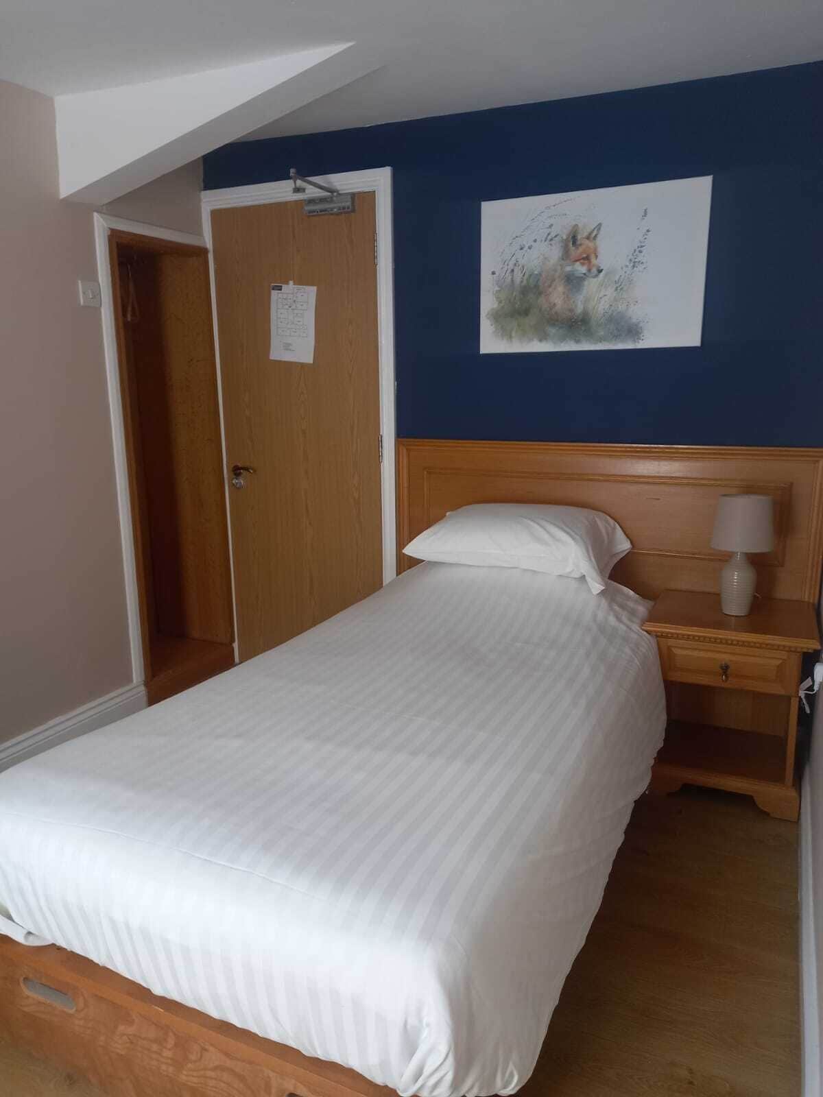 A bedroom with a wooden bed, a nightstand, a wall-mounted lamp, and a door with a note.