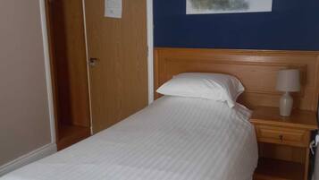 A bedroom with a wooden bed, a nightstand, a wall-mounted lamp, and a door with a note.