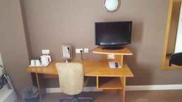 Een kamer met een houten bureau, een zwarte flatscreen-tv, een stoel, een prullenbak en een spiegel bevestigd aan de muur.