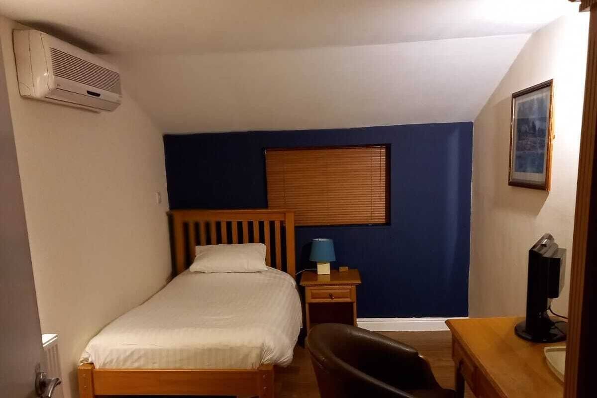 A small, well-lit room with a single bed, a desk, and a chair.