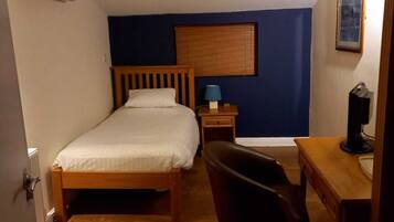 A small, well-lit room with a single bed, a desk, and a chair.