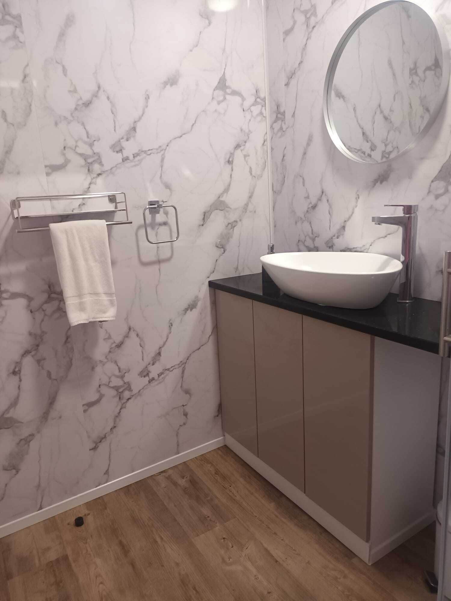 Un baño con pared de mármol, un espejo redondo, un lavabo blanco y un perchero para toallas.