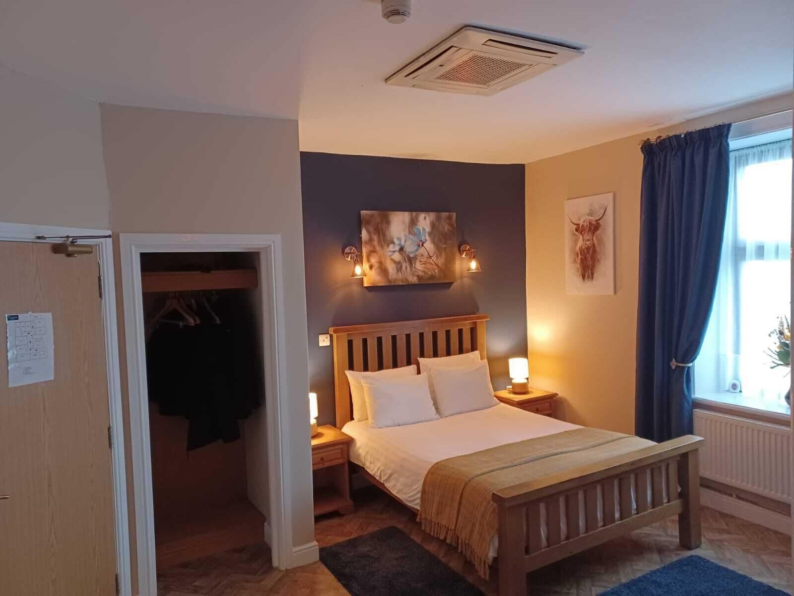 A bedroom with a wooden bed, bedside lamps, a painting, and a window with curtains.