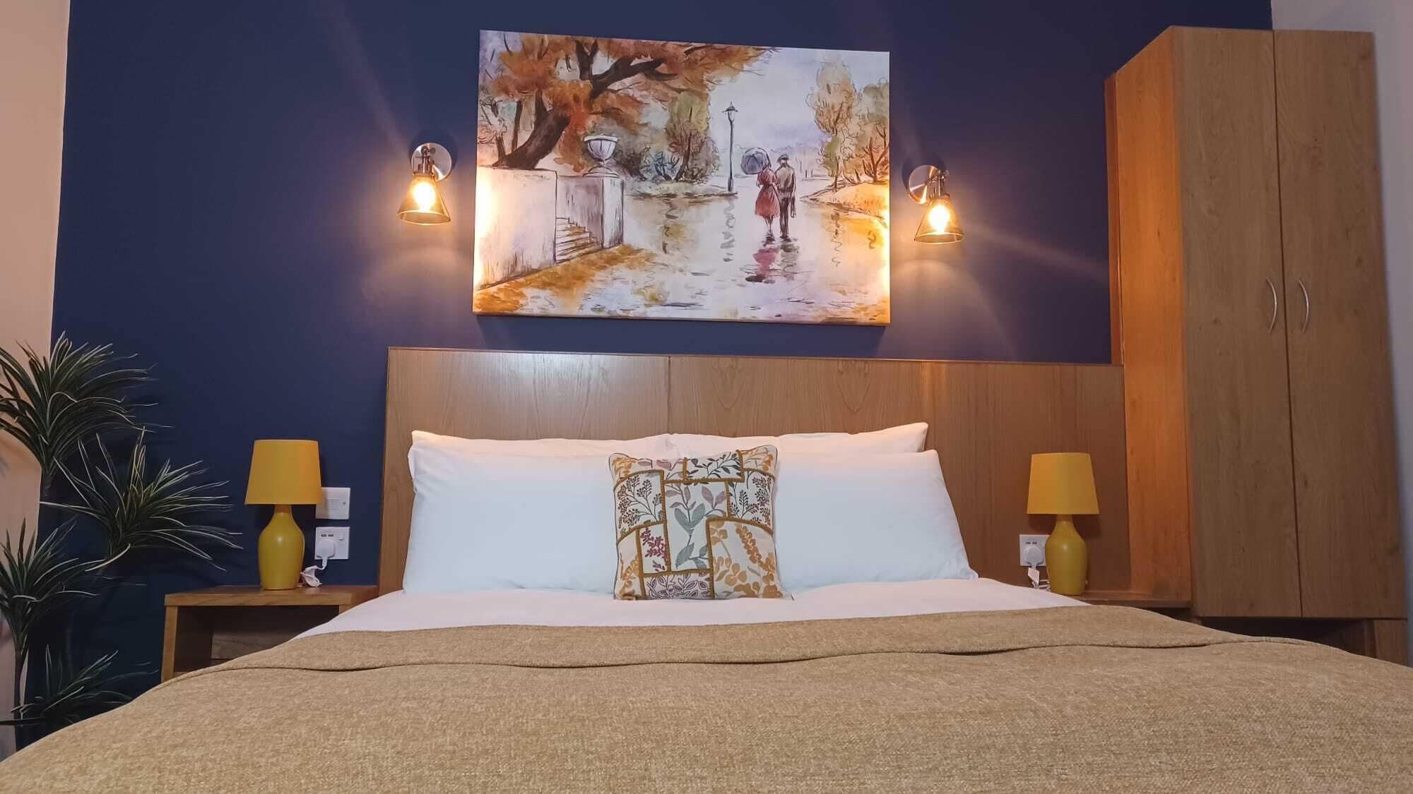 Habitación de hotel con cama, dos lámparas de noche, un cuadro en la pared y un armario de madera.
