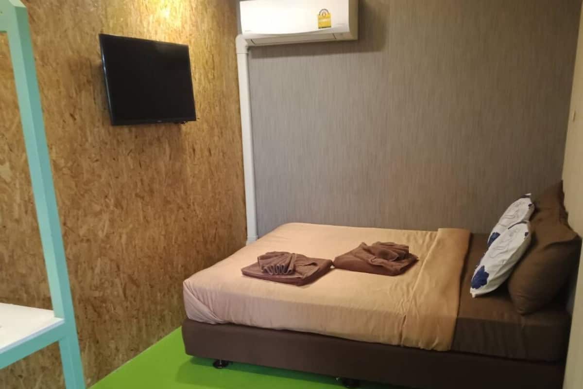 Una habitación con una cama, un televisor montado en la pared y un equipo de aire acondicionado.
