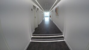 A long, narrow hallway with white walls and dark flooring, leading to a bright room at the end. - Terminal Hotel One (Sindelfingen)