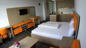 A hotel room with a bed, a desk with a chair, a TV, a small table with a vase of flowers, and a kitchenette. - Terminal Hotel One (Sindelfingen)