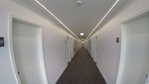A long, narrow hallway with white walls and dark flooring, leading to a door at the end. - Terminal Hotel One (Sindelfingen)