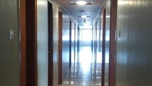 A long, narrow hallway with doors on both sides, leading to rooms. The floor is shiny and reflective, and the walls are a light color. - Hotel Sai Palace Express (Rahata)