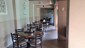 A spacious dining area with multiple tables and chairs, ceiling fans, and framed artwork on the walls. - Hotel Sai Palace Express (Rahata)