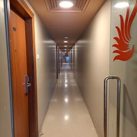 Un pasillo largo y estrecho con una puerta de madera a la izquierda y una pared de vidrio con un logotipo rojo a la derecha.