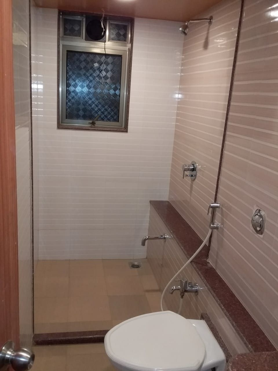 Un bagno con un WC, una doccia e una finestra con porta in vetro decorato.