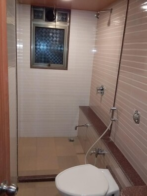 A bathroom with a toilet, a shower, and a window with a patterned glass door. - Hotel Sai Palace Express (Rahata)