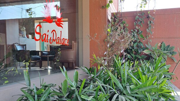 A hotel entrance with a 'Sai Palace' sign, a seating area with chairs and a table, and a large planter with green foliage. - Hotel Sai Palace Express (Rahata)