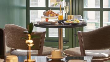 Comedor con una mesa lista para el desayuno, incluyendo croissants y fruta, con vista a la calle a través de grandes ventanales.