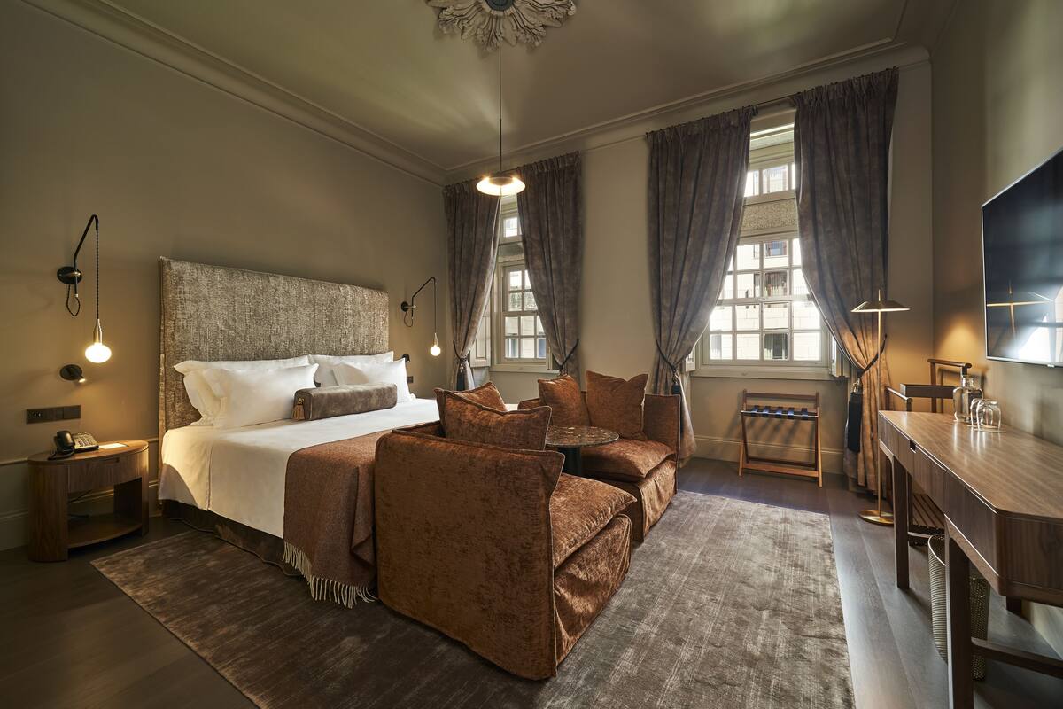 A hotel room with a large bed, brown upholstered seating, a desk, and a television.
